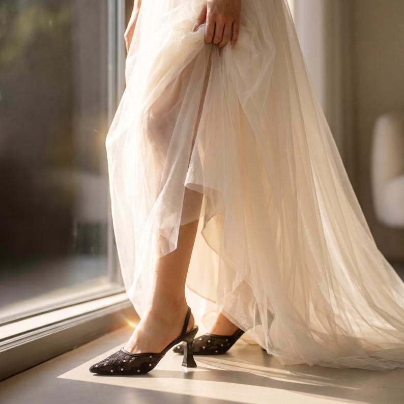 Elegant lace slingback heels with pointed toe and sculpted heel, available in white and black colors, styled in romantic bridal setting with pearls, lace fabric, and floral details for wedding or special occasion wear.