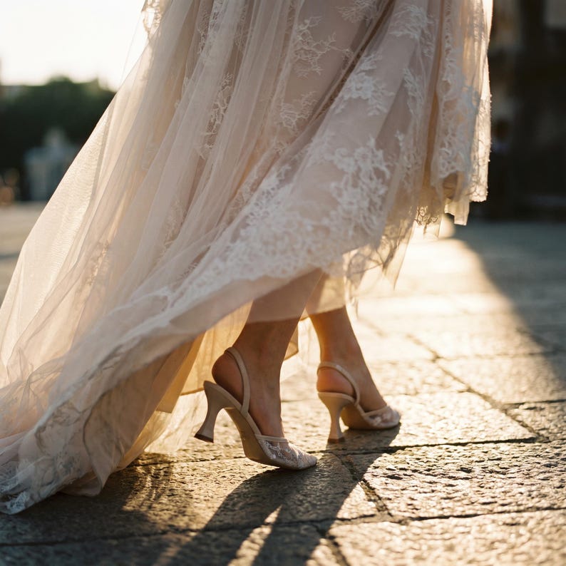 Elegant lace slingback heels with pointed toe and sculpted heel, available in white and black colors, styled in romantic bridal setting with pearls, lace fabric, and floral details for wedding or special occasion wear.