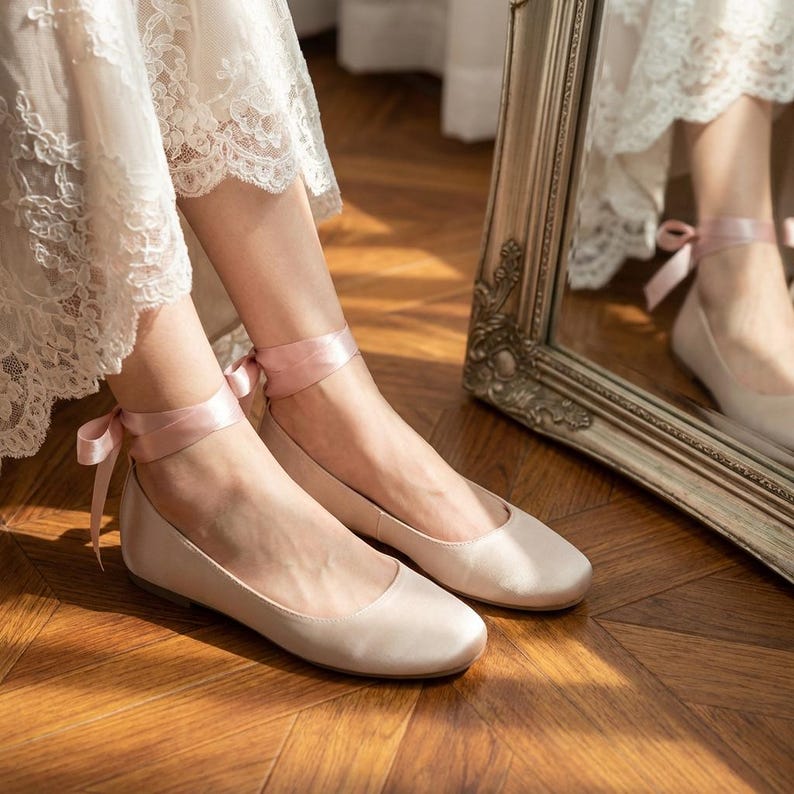 Bridal ballet flats with ribbon ties in soft blush satin, comfortable wedding shoes for bride, minimalist flat shoes for ceremony and reception, elegant lightweight bridal footwear on wooden floor
