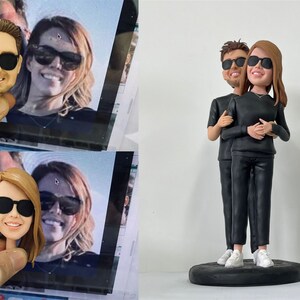 May include: A custom-made figurine of a couple wearing black clothing and sunglasses. The figurine is standing on a black circular base.