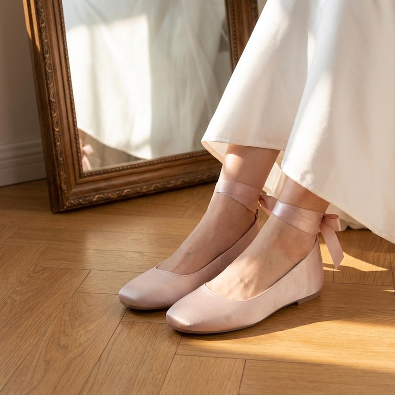 Bridal ballet flats with ribbon ties in soft blush satin, comfortable wedding shoes for bride, minimalist flat shoes for ceremony and reception, elegant lightweight bridal footwear on wooden floor