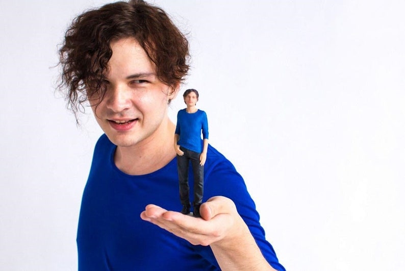 May include: A person holding a small blue figurine of another person in their hand. Both figures are wearing blue shirts.