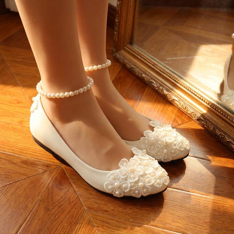 Ivory bridal lace flats with pearl details on feet, elegant wedding ballet shoes with floral lace design, comfortable bride shoes for ceremony and reception on wooden floor