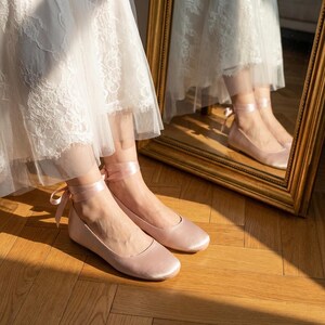 Bridal ballet flats with ribbon ties in soft blush satin, comfortable wedding shoes for bride, minimalist flat shoes for ceremony and reception, elegant lightweight bridal footwear on wooden floor