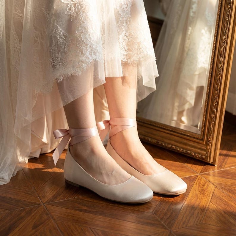Bridal ballet flats with ribbon ties in soft blush satin, comfortable wedding shoes for bride, minimalist flat shoes for ceremony and reception, elegant lightweight bridal footwear on wooden floor