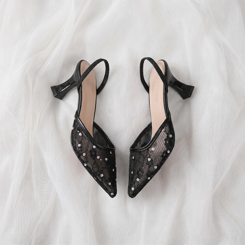 Elegant lace slingback heels with pointed toe and sculpted heel, available in white and black colors, styled in romantic bridal setting with pearls, lace fabric, and floral details for wedding or special occasion wear.