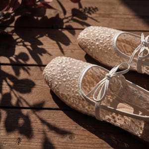 Delicate lace bridal flats with transparent floral mesh and strap styles, minimalist wedding ballet shoes in ivory tones, soft comfortable footwear for bride displayed on neutral fabric background, multiple elegant variations