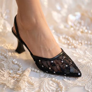 Elegant lace slingback heels with pointed toe and sculpted heel, available in white and black colors, styled in romantic bridal setting with pearls, lace fabric, and floral details for wedding or special occasion wear.