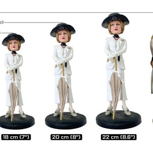 May include: Three figurines of a woman wearing a white dress and hat, holding an umbrella. The figurines are different sizes, with the largest being 8.6 inches tall and the smallest being 7 inches tall.  The text "Large (1/8th Scale)", "Medium (1/9th Scale)", and "Small (1/10th Scale)" is above the figurines.  A figurine of a man and woman standing together is to the right of the figurines.