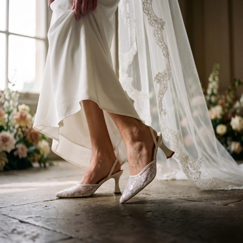 Elegant lace slingback heels with pointed toe and sculpted heel, available in white and black colors, styled in romantic bridal setting with pearls, lace fabric, and floral details for wedding or special occasion wear.
