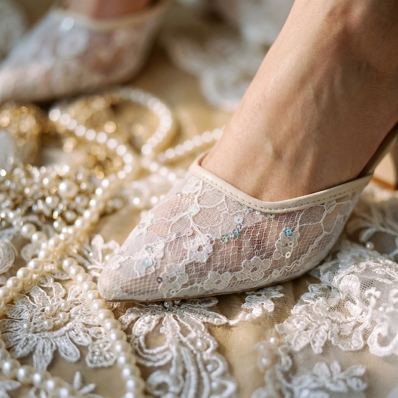 Elegant lace slingback heels with pointed toe and sculpted heel, available in white and black colors, styled in romantic bridal setting with pearls, lace fabric, and floral details for wedding or special occasion wear.