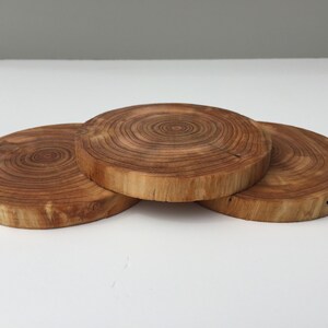 Könnte beinhalten: Drei runde Holz-Untersetzer mit natürlicher Holzoptik. Die Untersetzer haben ein kreisförmiges Maserungsmuster.