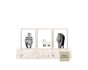 May include: Three framed wall art prints in light wood frames. The left print shows the rear of a zebra, the center print features the black text "Nice BUM" on a white background, and the right print displays the rear of an elephant in black and white.