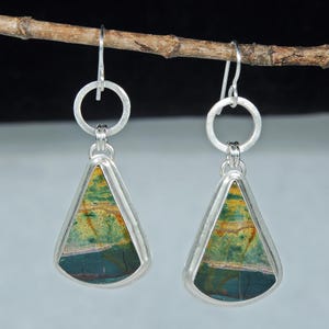 May include: A pair of dangle earrings featuring triangular-shaped stones with horizontal bands of green, yellow, and dark red. Each stone is set in a silver-toned metal frame, suspended from a silver-toned circular link and a silver-toned hook wire.
