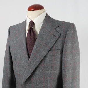 Puede incluir: Una chaqueta gris de doble botonadura con un estampado de cuadros rojos y blancos. La chaqueta tiene solapa de muesca y cierre de un solo botón.