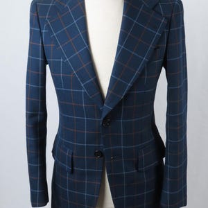 May include: A navy blue blazer with a plaid pattern in shades of brown and light blue. The blazer has a two-button closure, notched lapels, and two front pockets. The jacket is displayed on a mannequin.