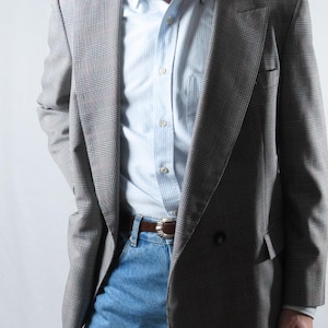 May include: A grey plaid blazer with a double-breasted design, worn with a light blue striped shirt and blue jeans. The blazer has a classic pattern and tailored fit. A brown leather belt completes the outfit. The blazer's length is approximately 76 cm.