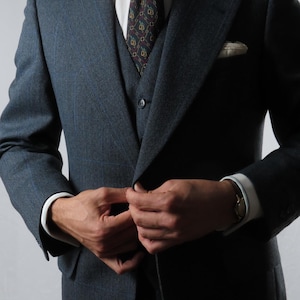 Pode incluir: Um fato de três peças azul-escuro com riscas, composto por um casaco de abotoamento simples, um colete a condizer, uma camisa branca com colarinho redondo e uma gravata escura com padrão e um lenço de bolso branco no bolso do peito.
