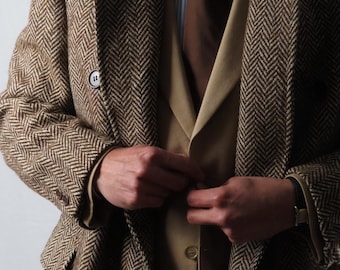Op de afbeelding: Een bruine visgraat tweed jas met bijpassend vest en stropdas. De jas heeft een klassiek ontwerp met een revers en knoopsluiting. Het vest is effen beige van kleur en de stropdas is donkerbruin. Het overhemd is blauw en wit gestreept.