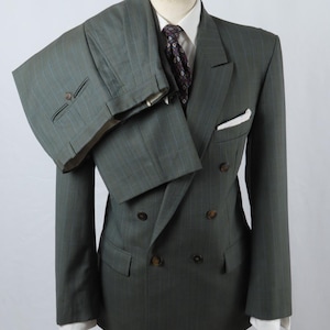 Puede incluir: Un traje cruzado de color verde oscuro con rayas diplomáticas y pantalones a juego colocados sobre el hombro, combinado con una camisa blanca de cuello, una corbata oscura estampada y un pañuelo de bolsillo blanco sobre un maniquí.