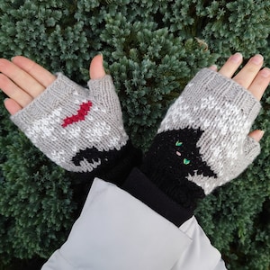 May include: A pair of grey and white fingerless gloves with black cat designs. One glove has a red heart on the cat's chest, and the other has green eyes.
