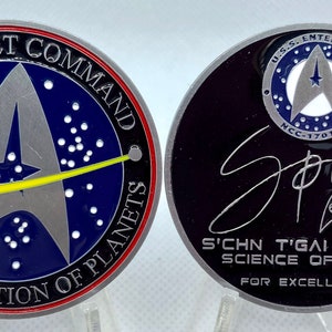 May include: A silver coin with a blue and yellow Starfleet emblem on one side and a black side with the signature of Spock, the text "S'CHN T'GAI SPOCK SCIENCE OFFICER FOR EXCELLENCE" and the text "U.S.S. ENTERPRISE NCC-1701-A" on the other side.