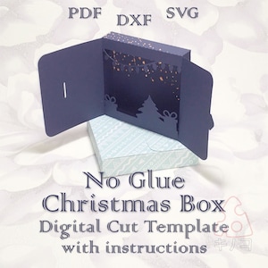 May include: A navy blue Christmas box digital cut template with instructions. The box features a cut-out Christmas tree and gift design, with a string of lights. The text "No Glue Christmas Box" is visible.