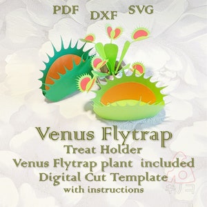 May include: Two green Venus flytrap treat holders with orange interiors. The holders are made of paper and are designed to look like Venus flytraps. A small Venus flytrap plant is included in the image. The image also includes the text "Venus Flytrap Treat Holder Venus Flytrap plant included Digital Cut Template with instructions".