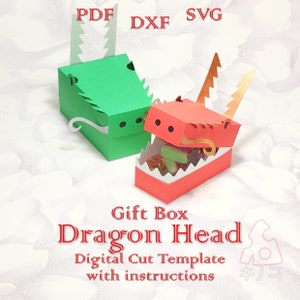 Könnte beinhalten: Zwei Geschenkkisten in Form eines Drachenkopfes, eine grün und eine rot, mit Süßigkeiten in der roten Kiste. Die Kisten sind aus Papier und haben einen 3D-Effekt. Der Text "Gift Box Dragon Head Digital Cut Template with instructions" befindet sich unter den Kisten.