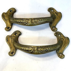 Peut inclure: Deux poignées de porte en laiton antique avec des motifs floraux ornés. Les poignées sont de style vintage et ont une finition légèrement ternie.
