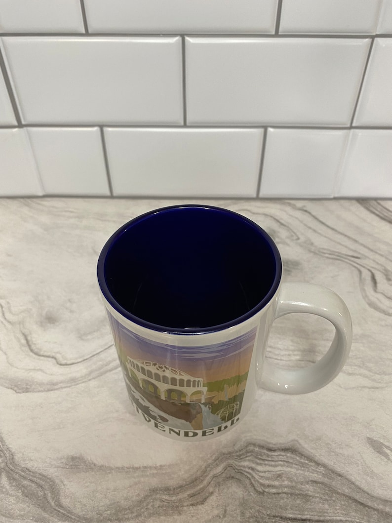 May include: White ceramic coffee mug with a blue rim and a colorful image of a building with the word "WENDEL" printed on the bottom.
