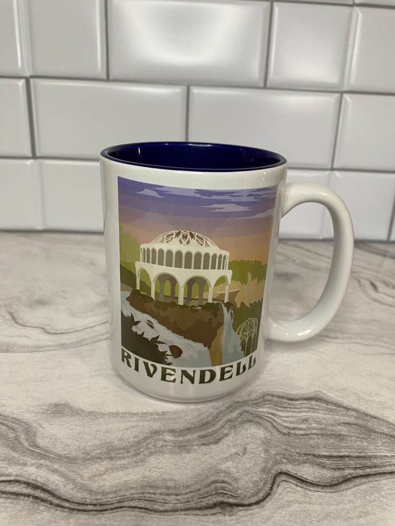 May include: White ceramic mug with a blue rim. The mug features a graphic of a building with a dome and a waterfall. The text "Rivendell" is printed on the bottom of the mug.
