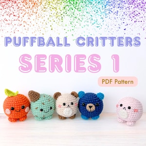 以下が含まれることがあります： オレンジ、緑、ベージュ、青、ピンクなど、さまざまな色の、かぎ針編みのパフボールの生き物5体のコレクション。各生き物には、クマの顔や葉っぱのついたオレンジなど、ユニークな特徴があります。「PUFFBALL CRITTERS SERIES 1」の文字が生き物の上に表示されています。
