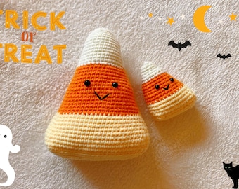 Pode incluir: Dois peluches de milho doce de crochê com rostos sorridentes. O peluche maior é laranja e branco, e o menor é laranja, branco e amarelo. Os peluches estão sobre uma superfície branca e fofa com o texto "Trick or Treat" em letras laranja na parte superior da imagem.