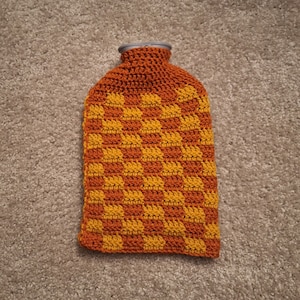 May include: A crocheted hot water bottle cover with a checkered pattern in orange and yellow.