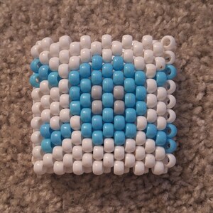 May include: A white and blue beaded bracelet with a geometric pattern. The bracelet is made of small, round beads that are strung together on a string.