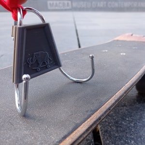 May include: A silver hook with a grey plastic tag featuring a small elephant design is attached to a wooden skateboard.