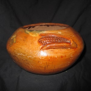 Puede incluir: Un cuenco de cerámica marrón con un diseño en relieve de una mazorca de maíz. El cuenco tiene un aspecto rústico y artesanal.