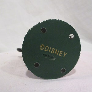 Puede incluir: La parte inferior de una figurita verde con un copyright de Disney en dorado y una etiqueta que dice "Hecho en China".