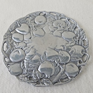 May include: A silver metal serving tray with a decorative design of apples and leaves. The tray has a scalloped edge and is perfect for serving fruit or snacks.