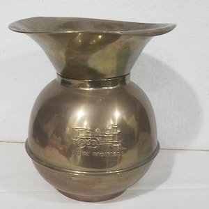 May include: A brass-colored, vintage-style pitcher with a wide, flared rim and a bulbous body. The pitcher features an embossed image of a train and the words "UNION PACIFIC" below the train image.