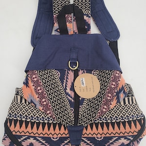 May include: A navy blue backpack with a colorful geometric pattern in shades of peach, purple, and cream. The backpack has adjustable straps, a zippered main compartment, and a flap closure with a metal clasp. A tag reads "Handmade with Love."