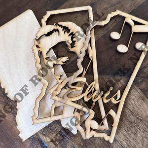 Peut inclure: Trois d&eacute;coupes en bois, l'une avec une silhouette d'Elvis Presley, l'autre avec le texte "King of Rock 'n' Roll", et la derni&egrave;re avec des notes de musique.