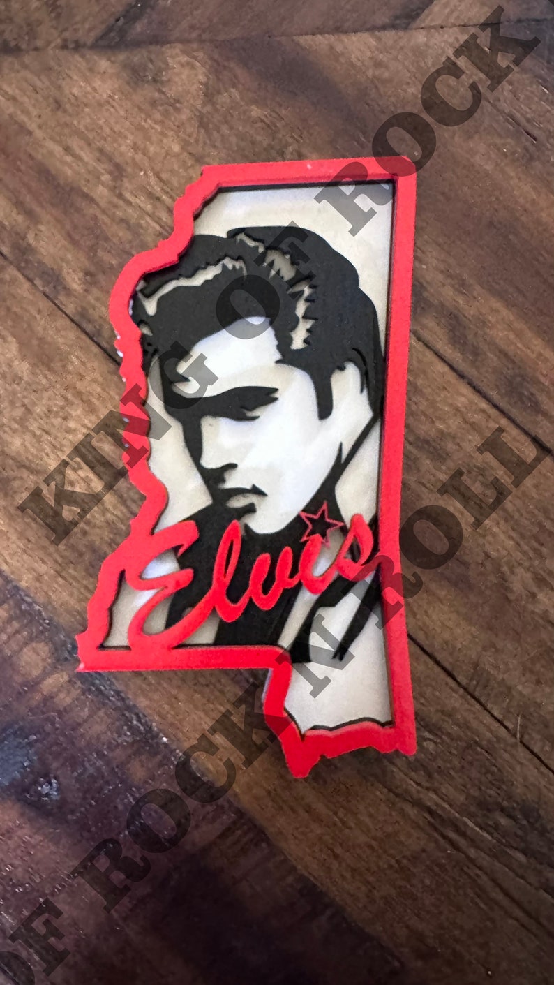 Peut inclure: Une d&eacute;coupe en bois rouge et blanche du visage d'Elvis Presley en forme de l'&eacute;tat du Mississippi. La d&eacute;coupe pr&eacute;sente une image en noir et blanc du visage d'Elvis Presley avec le mot "Elvis" &eacute;crit en rouge sous l'image.
