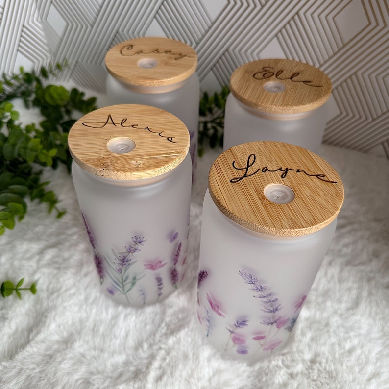 May include: Four frosted glass jars with bamboo lids. Each lid has a different name engraved on it: Casey, Elle, Alexia, and Layne. The jars have a floral design with purple and pink flowers.