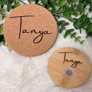 May include: Two round, personalized coasters. One is made of cork and the other is made of bamboo. Both coasters feature the name "Tanya" engraved in a cursive font.