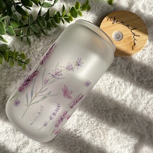 May include: A frosted glass jar with a floral design featuring lavender and other flowers. The jar has a wooden lid with the word "Geraldine" written on it.