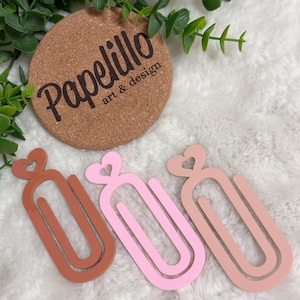 May include: Three decorative paper clips with heart-shaped tops. The paper clips are in brown, pink, and light pink.