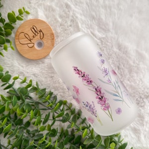 May include: A frosted glass tumbler with a floral design featuring lavender flowers and leaves. The tumbler has a wooden lid with the name "Shelly" engraved on it.