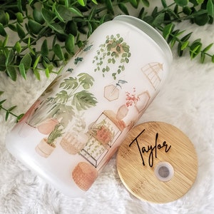May include: A white ceramic tumbler with a watercolor design of plants and a bamboo lid with the name "Taylor" engraved on it.